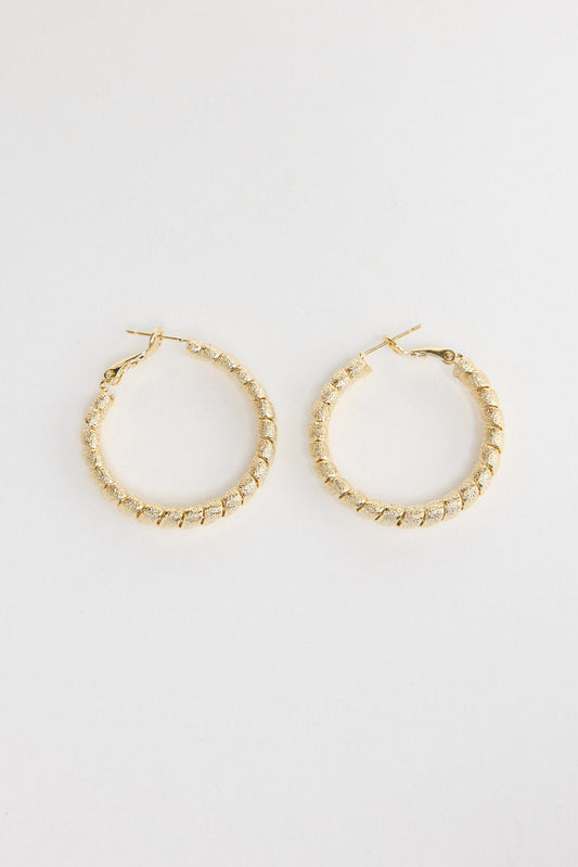 Neela Earrings in Gold – twisted, textured gold-tone hoop earrings shown flat on a white background.